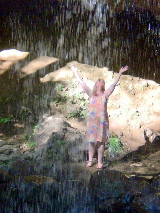 woman with raised arms, under waterfall